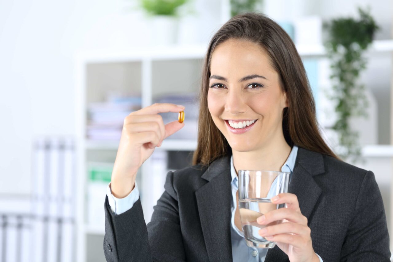 žena v pracovním prostředí s pilulkou a sklenicí vody